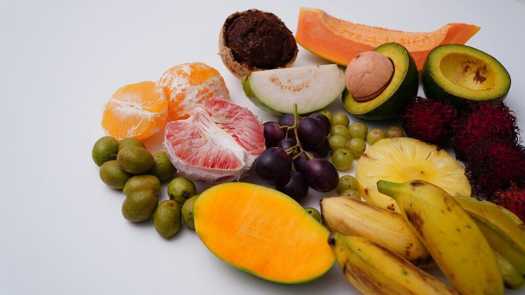 An assortment of colorful tropical fruits including mango, papaya, avocado, grapes, rambutan, bananas, grapefruit, and an orange.