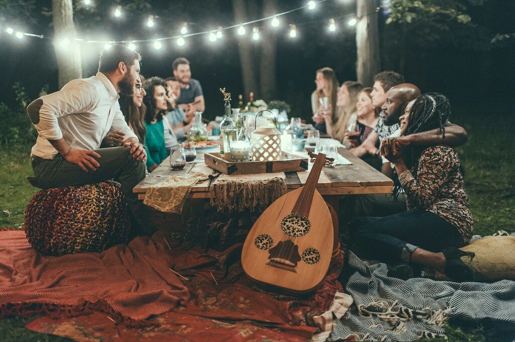 Friends at an outdoor dinner party with string lights and a lute.