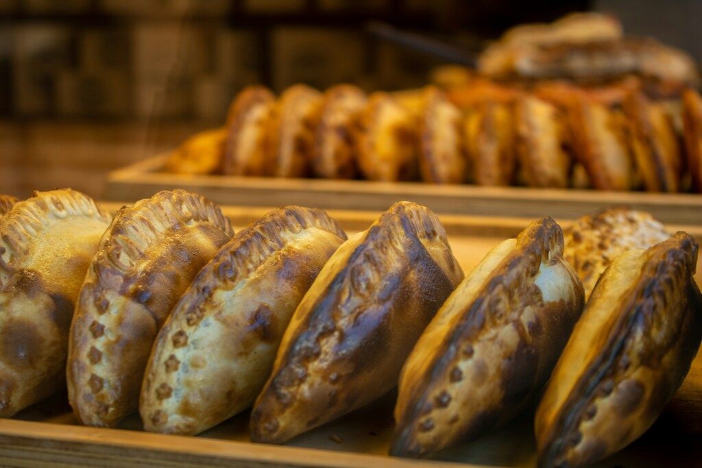 Rows of freshly baked golden-brown empanadas on wooden trays.