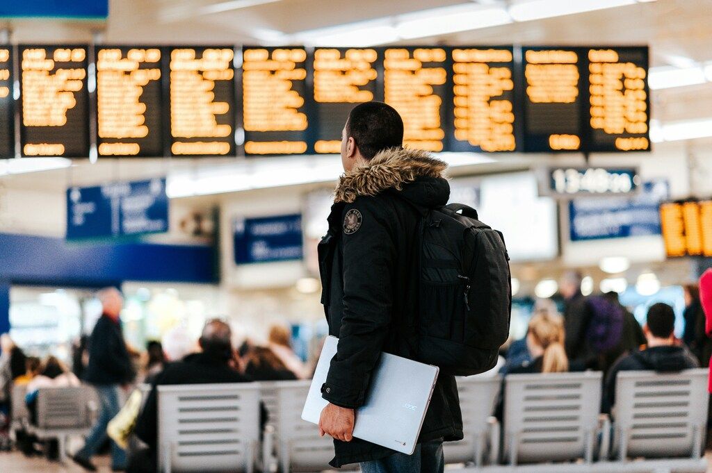 Man with laptop and backpack checking airport departure boards.