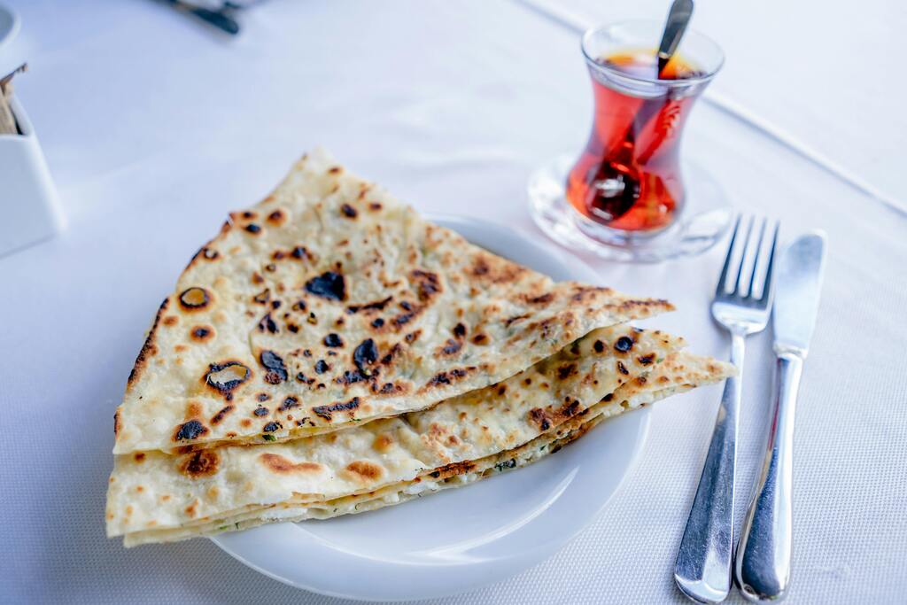 A plate with several folded flatbreads (gozleme) and a glass of Turkish tea in the background.
