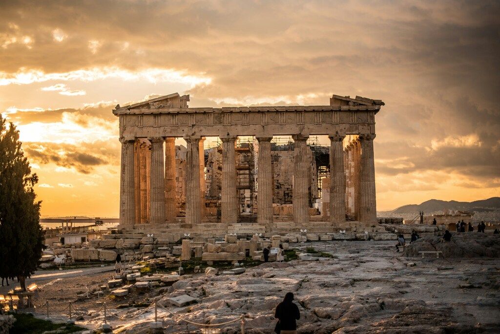 The ancient Parthenon temple on the Acropolis in Athens, Greece, illuminated by the warm light of a sunset, with people exploring the site.
