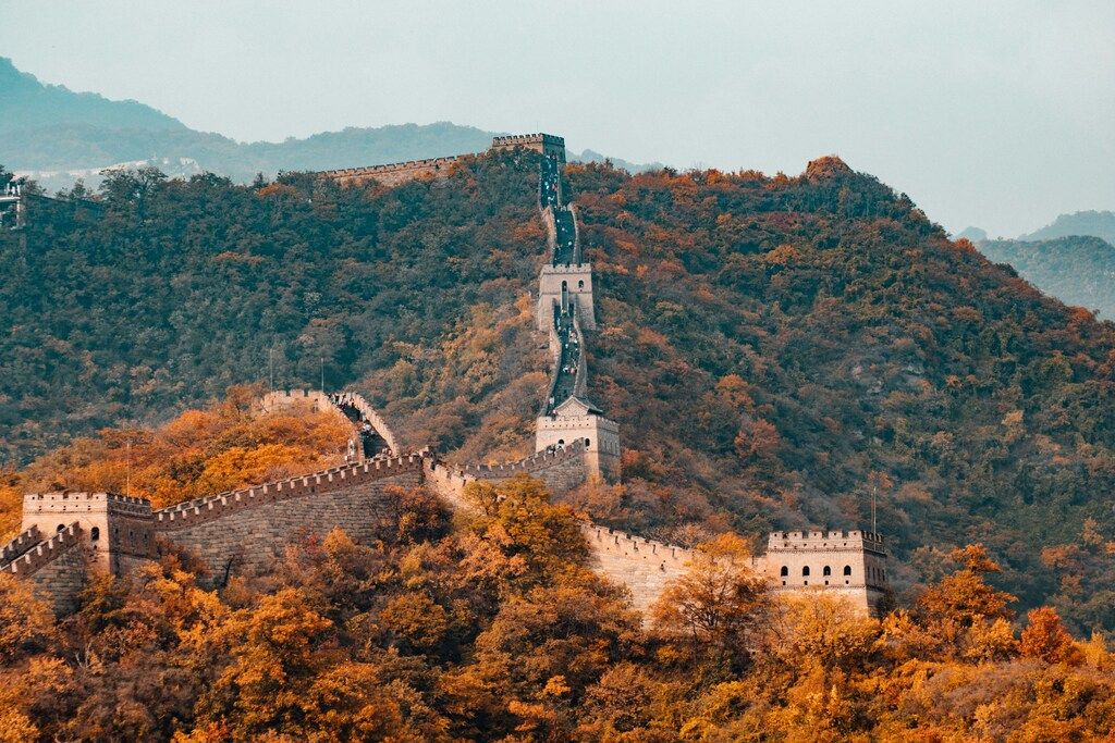 The Great Wall of China stretching across lush, autumn-colored mountains under a soft sky.