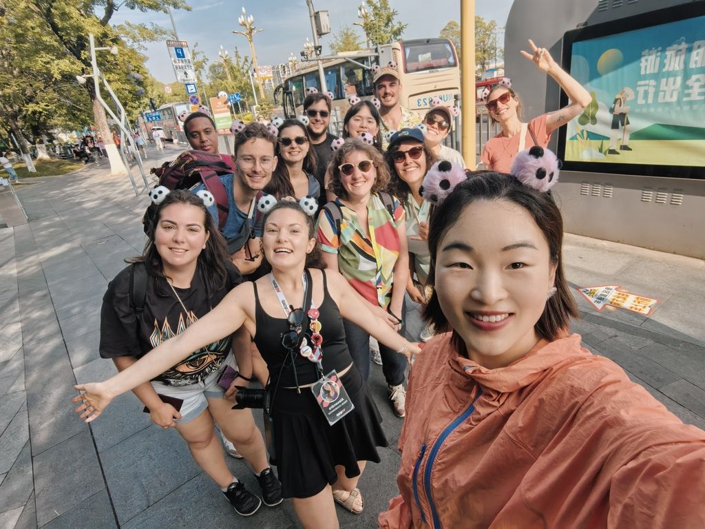 A group of WeRoad travelers smiling and posing for a selfie on a street in China, many wearing panda-ear headbands.