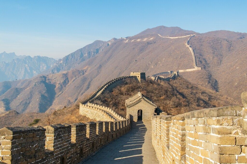 The Great Wall of China winding along rugged mountain ridges under a clear blue sky.