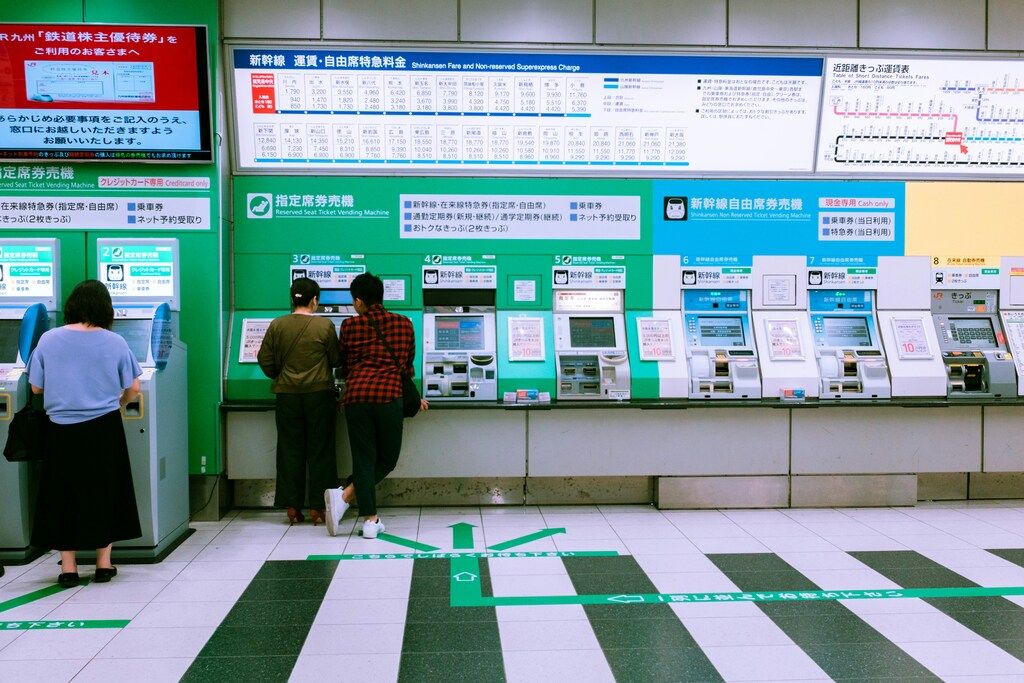 People using automated ticket vending machines for Shinkansen and other train services at a Japanese station.