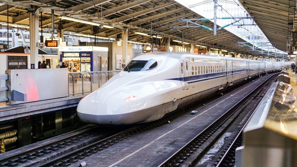 High-speed Shinkansen train arriving at a modern platform in Japan, with shops and digital signs in the background.
