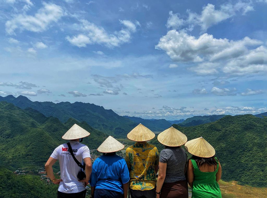 Group of travelers wearing Vietnamese conical hats enjoying a panoramic mountain view in Vietnam on a WeRoad group trip.