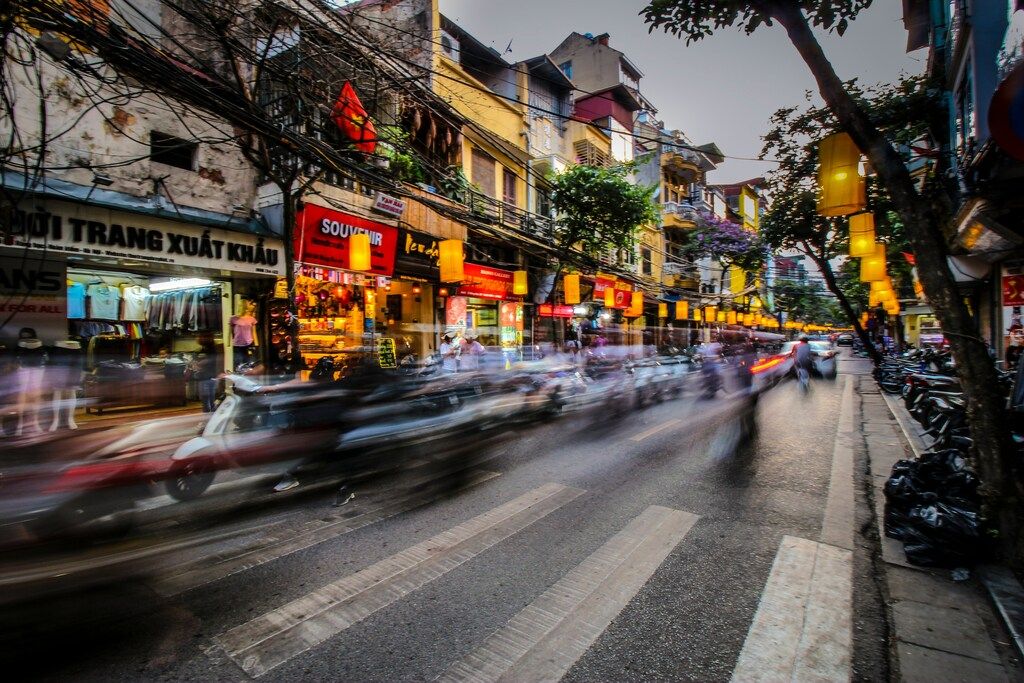 Busy Hanoi street at twilight with blurred motion of motorbikes and glowing shop signs.