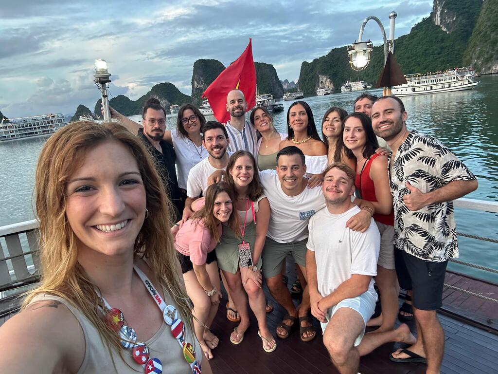 WeRoad travelers posing for a selfie on a boat in Ha Long Bay, with limestone karsts and cruise boats in the background.