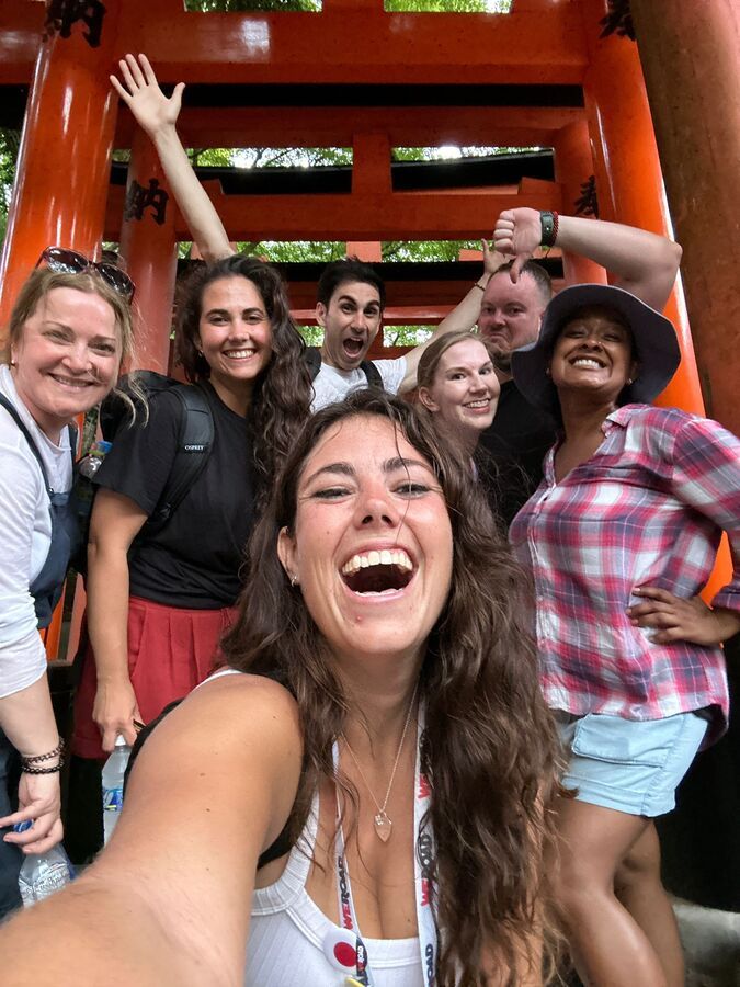 Smiling WeRoad group posing for a selfie under the red torii gates at Fushimi Inari Shrine in Kyoto.