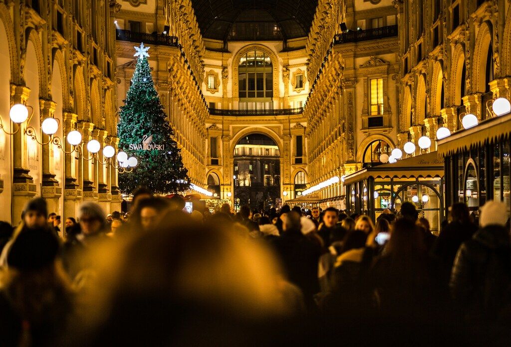 Crowded interior of the Galleria Vittorio Emanuele II in Milan, adorned with Christmas lights and a large Swarovski tree.