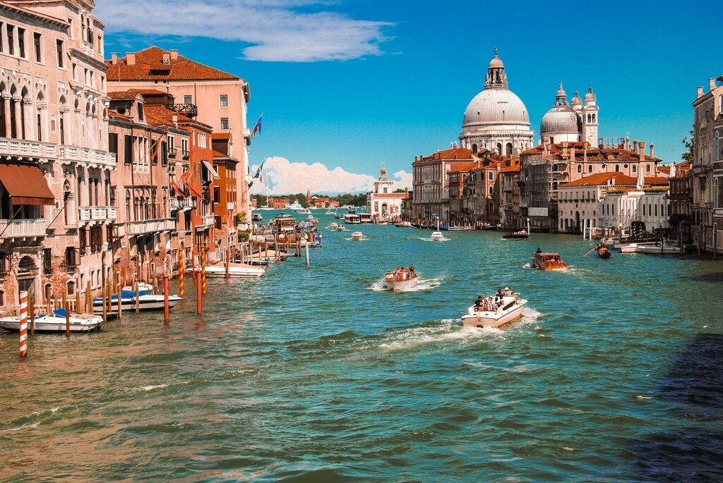 Boats cruising along the Grand Canal in Venice, with historic buildings and the domes of Santa Maria della Salute in the background.