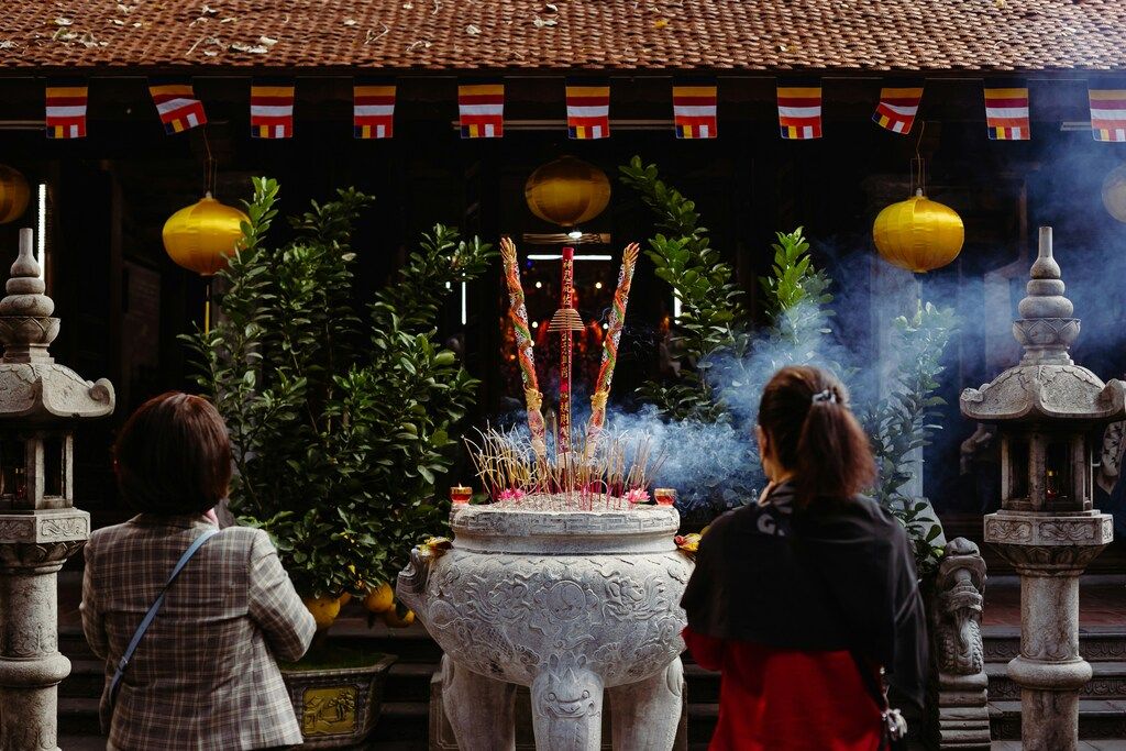 Two women standing in front of a large incense burner with smoke rising at a traditional Vietnamese temple.