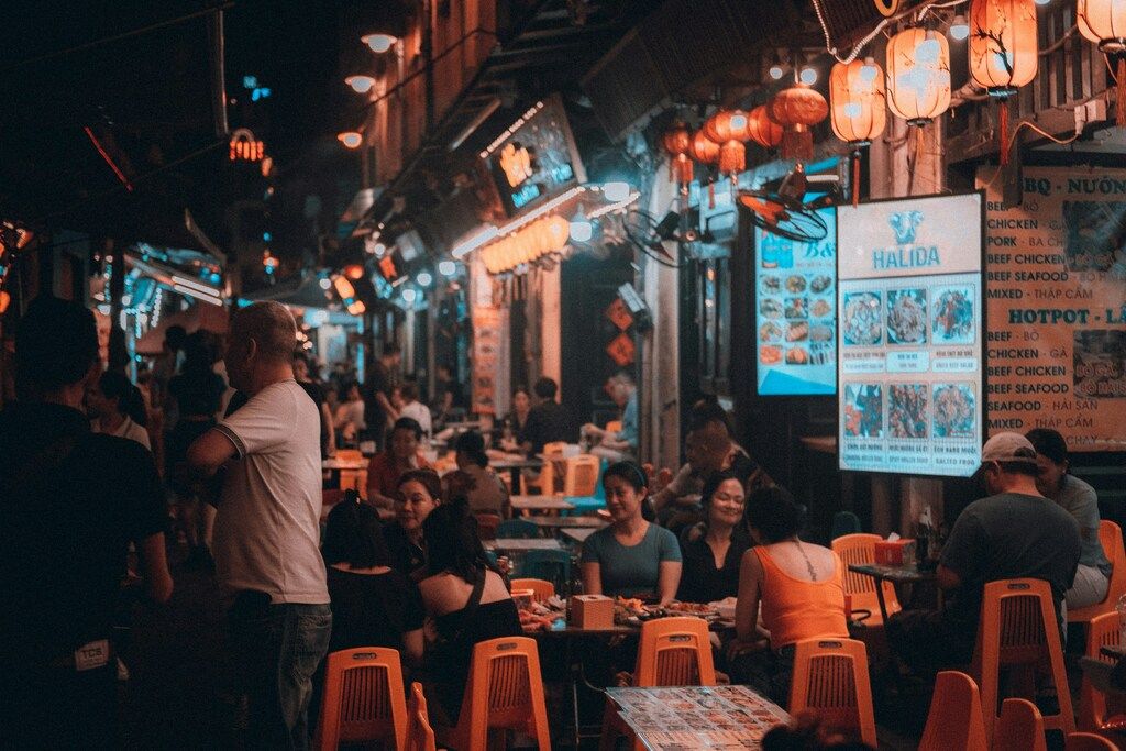 Crowded street food market in Vietnam at night with locals and tourists dining under lantern lights.
