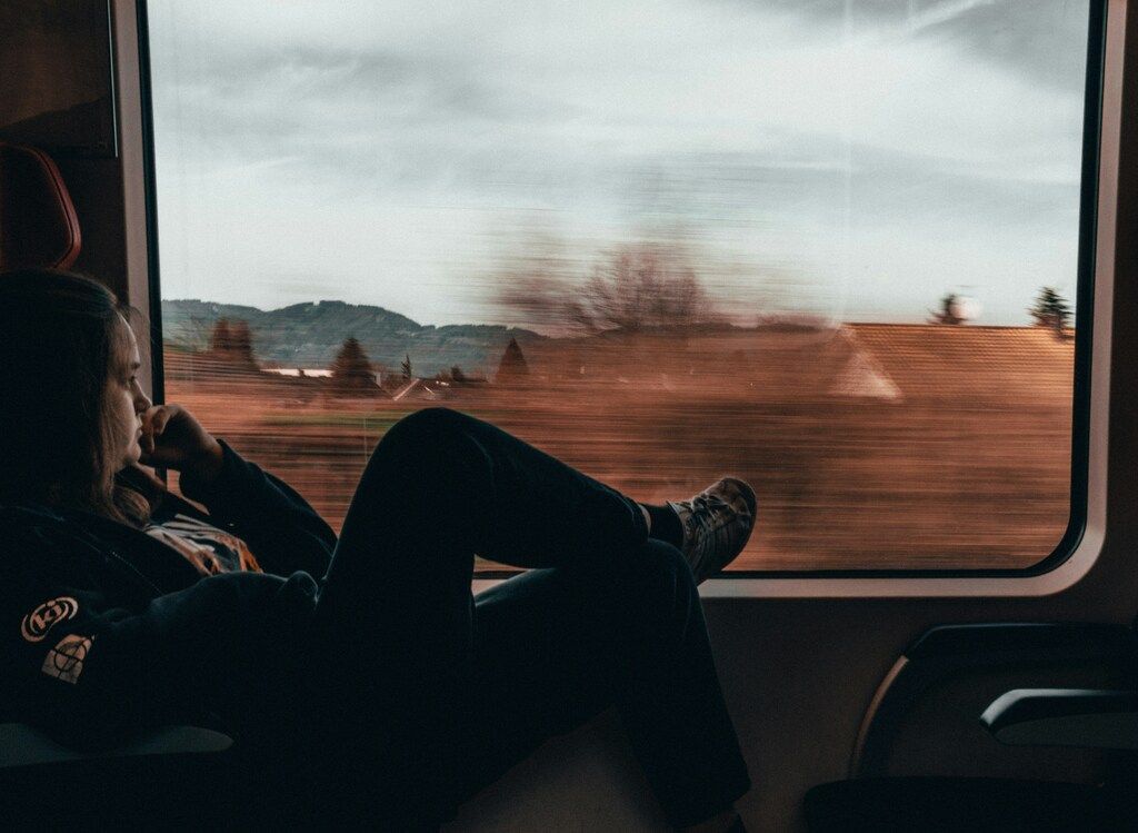 A passenger sitting with legs up by a train window, watching a blurred countryside landscape speed by.