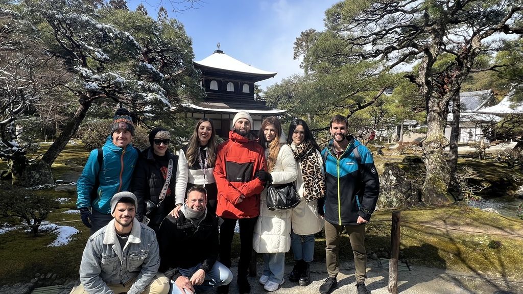 WeRoad group trip in Japan: smiling travelers in front of a snowy temple garden
