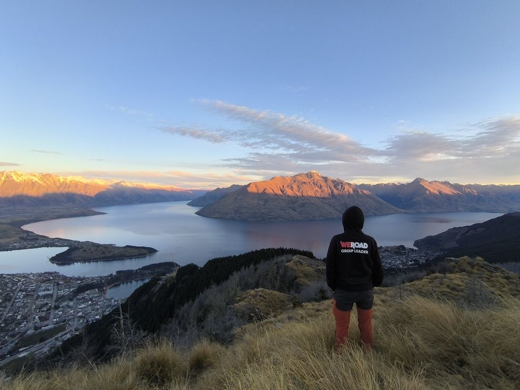 Traveler wearing a WeRoad hoodie overlooking Lake Wakatipu at sunrise in Queenstown, New Zealand.