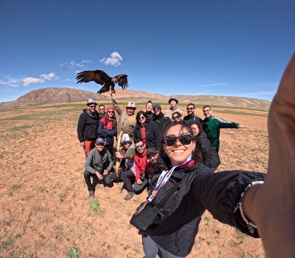Les voyageurs de WeRoad posent pour un selfie avec un aigle chasseur dans le désert montagneux du Kirghizistan.