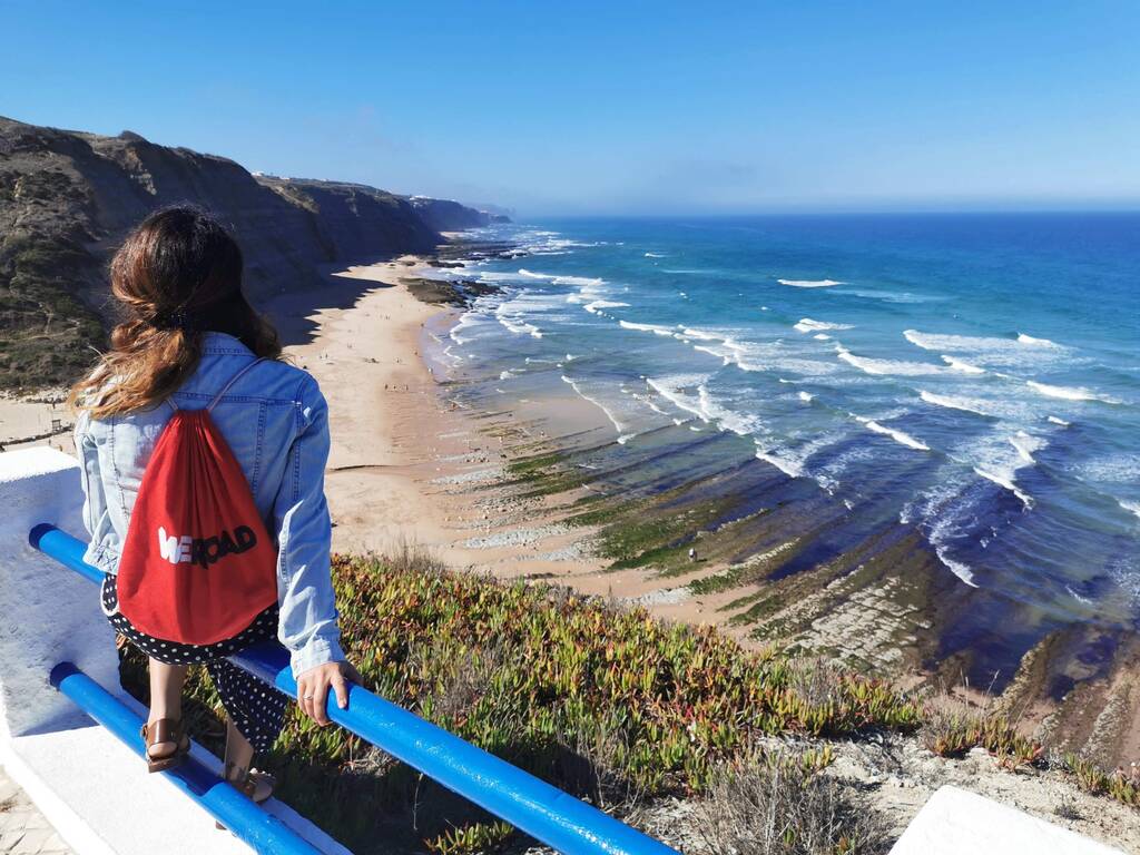 Solo traveler with a WeRoad red backpack admiring the coastline in Azenhas do Mar, Portugal.