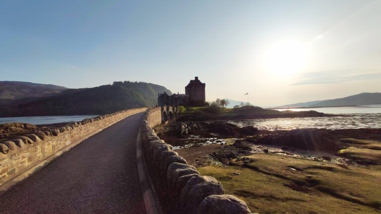 Urquhart Castle on the shores of Loch Ness, with a stone bridge leading to the historic Scottish ruin under a bright sky.