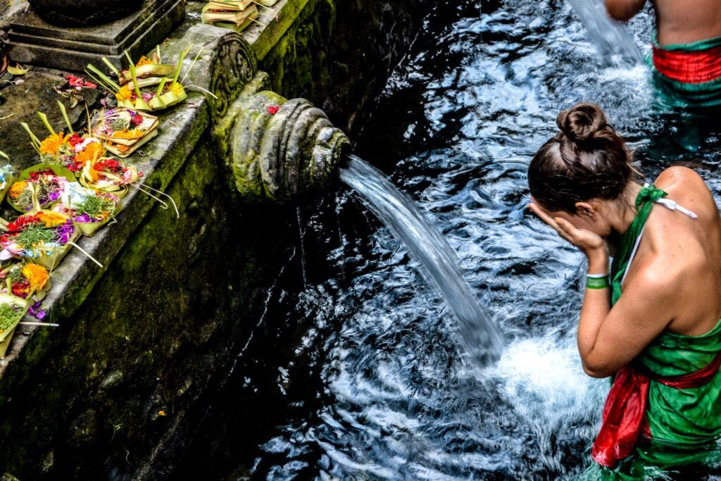 Woman praying under water spigot at Tirta Empul temple in Bali.