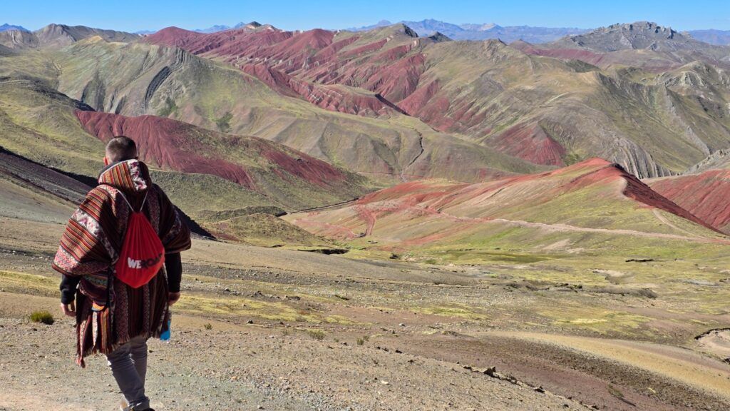 Hiker wearing a traditional South American poncho overlooking vast, multicolored mountain ridges in the Peruvian Andes.