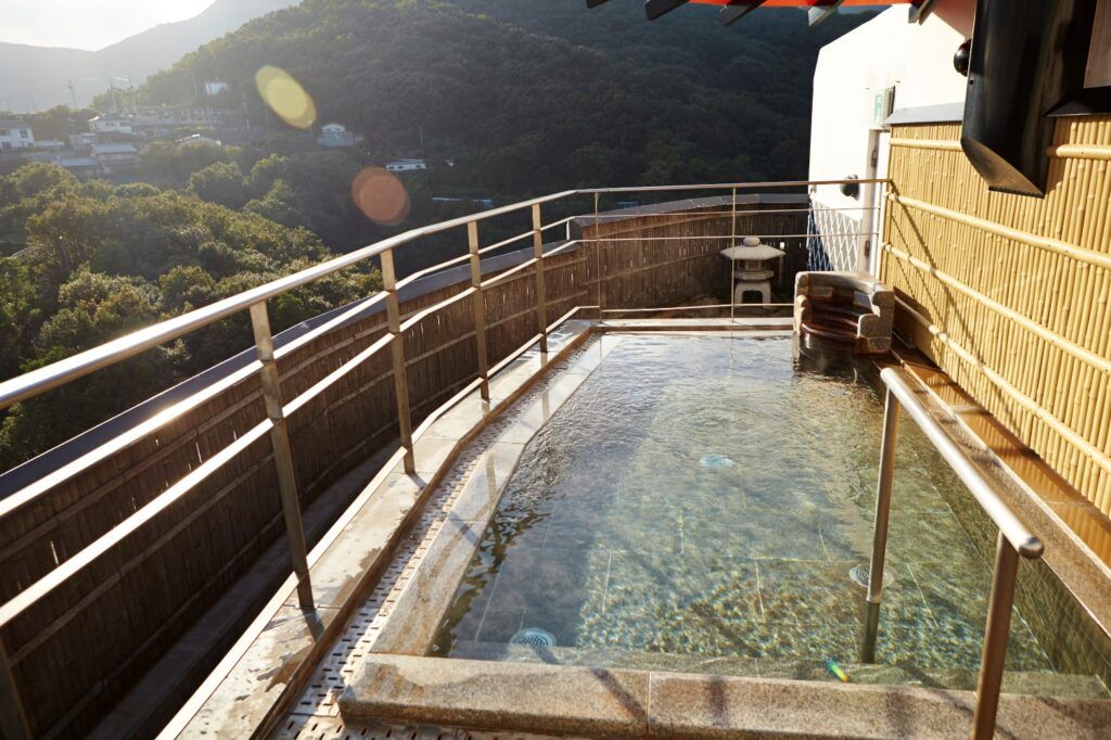 Outdoor private onsen bath on a balcony overlooking forested mountains.