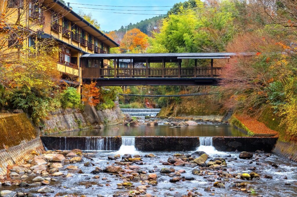 Traditional Japanese ryokan bridge over a river during autumn foliage.