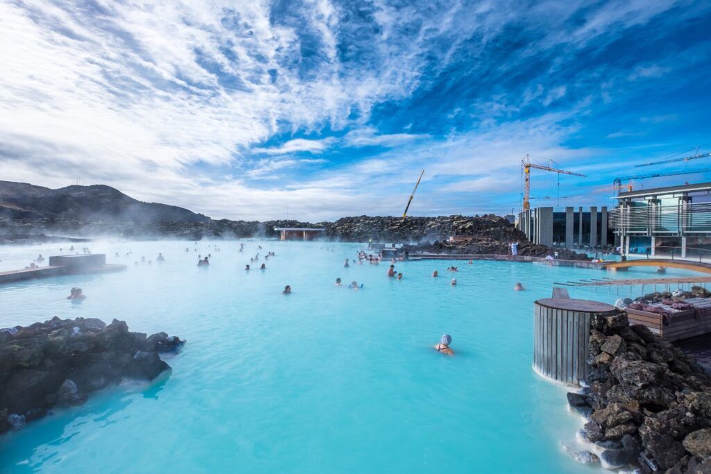 People bathing in Iceland's geothermal Blue Lagoon, with turquoise water and steam under a blue sky.