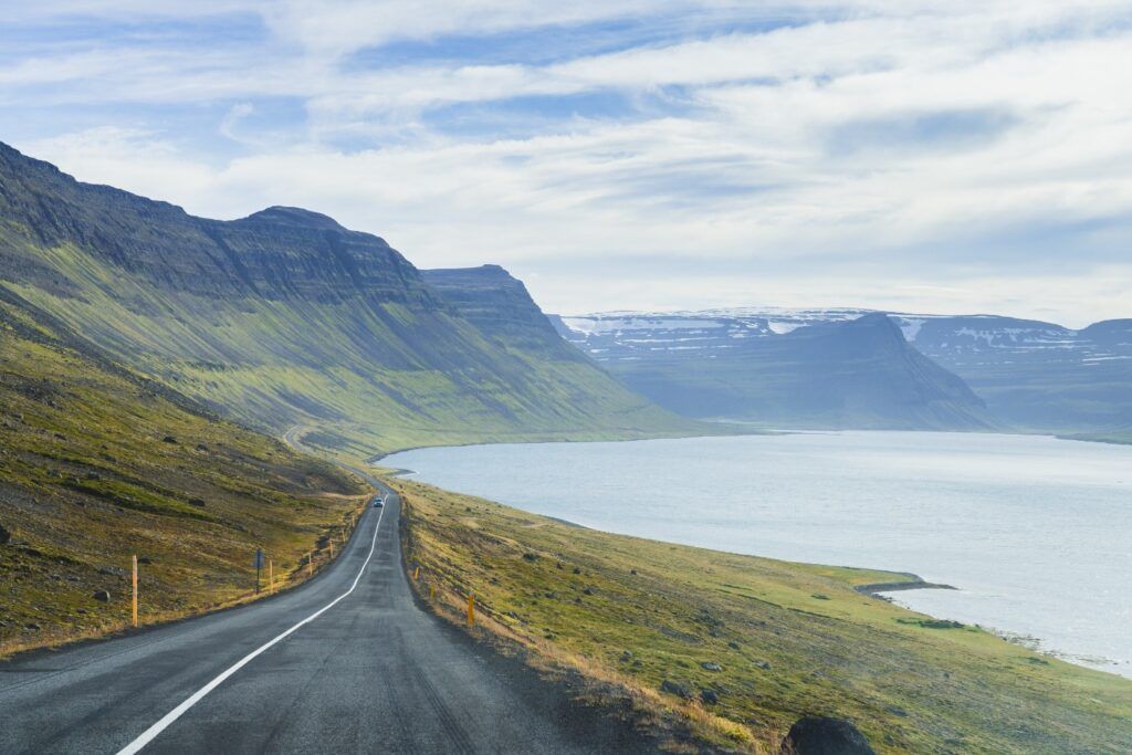 Scenic long road winding along a fjord between green hills in Westfjords.