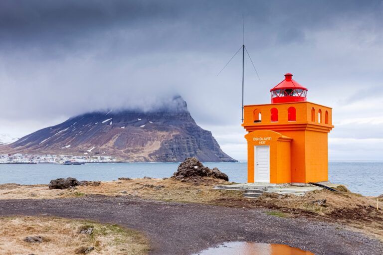 Orange lighthouse with mountain in background near Ísafjörður.