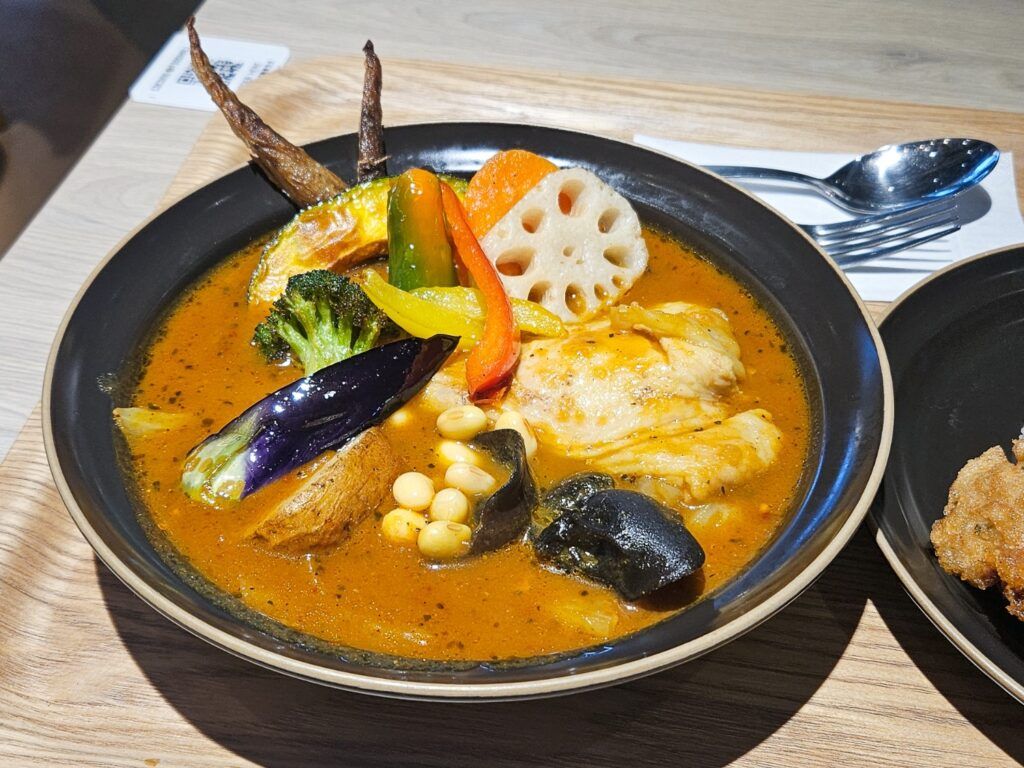 A bowl of spicy Soup Curry from Sapporo, filled with chicken, vegetables, and lotus root