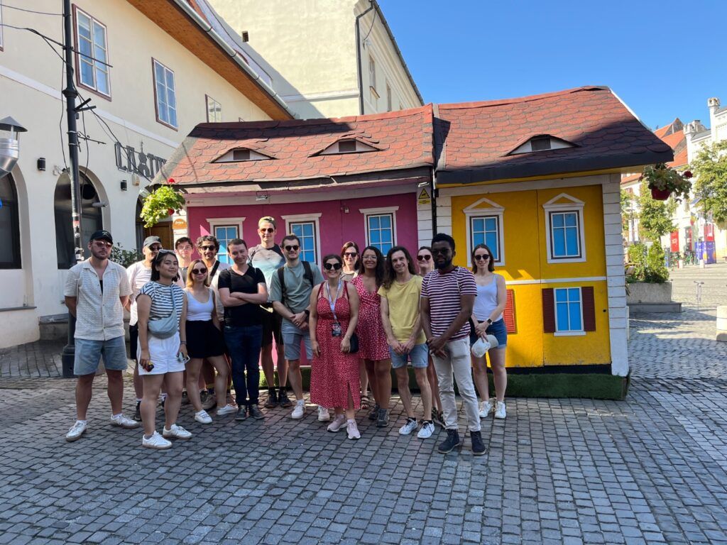 A cheerful group of WeRoad travelers posing in front of the “houses with eyes” in Sibiu, Romania.