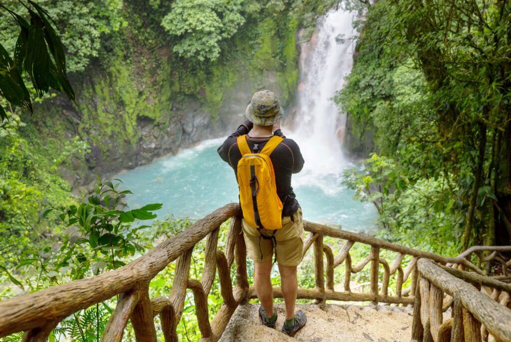 Hiker viewing a turquoise waterfall and pool from an observation deck.