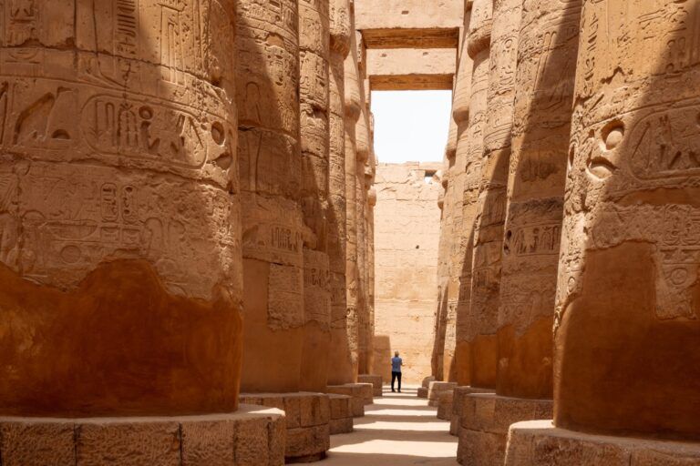 Sunlit corridor between rows of monumental, hieroglyph-covered columns in the Great Hypostyle Hall of the Temple of Karnak, Egypt.