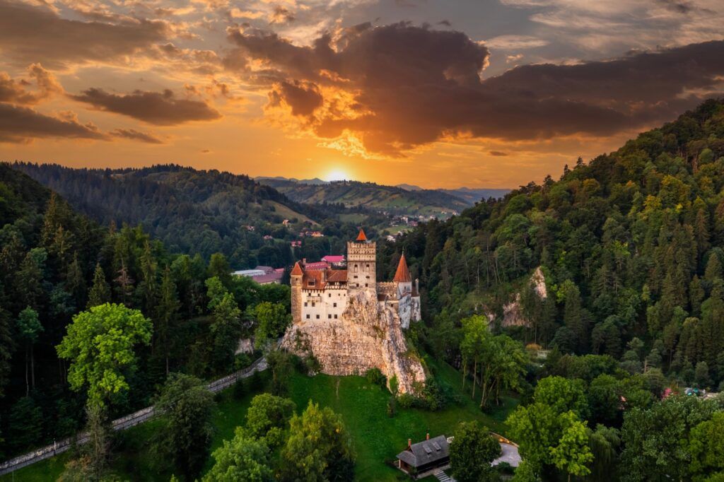 Dramatic sunset view of Bran Castle nestled in the green hills of Transylvania.