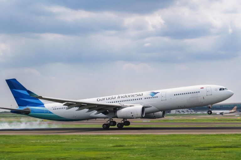 A Garuda Indonesia Airbus A330 landing on a runway, touching the ground and a cloudy sky in the background.