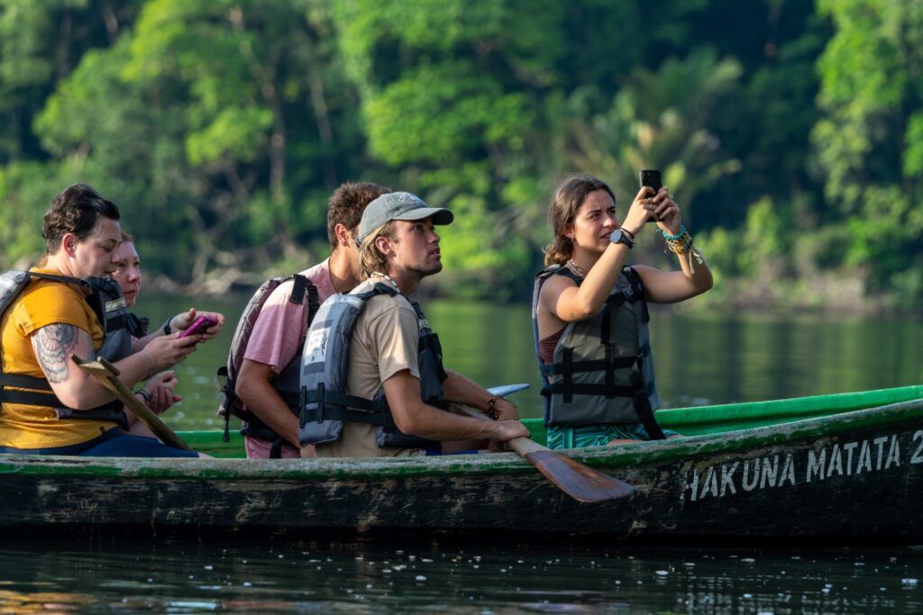 Group of WeRoad travelers in a narrow boat (canoe), paddling on a jungle river.