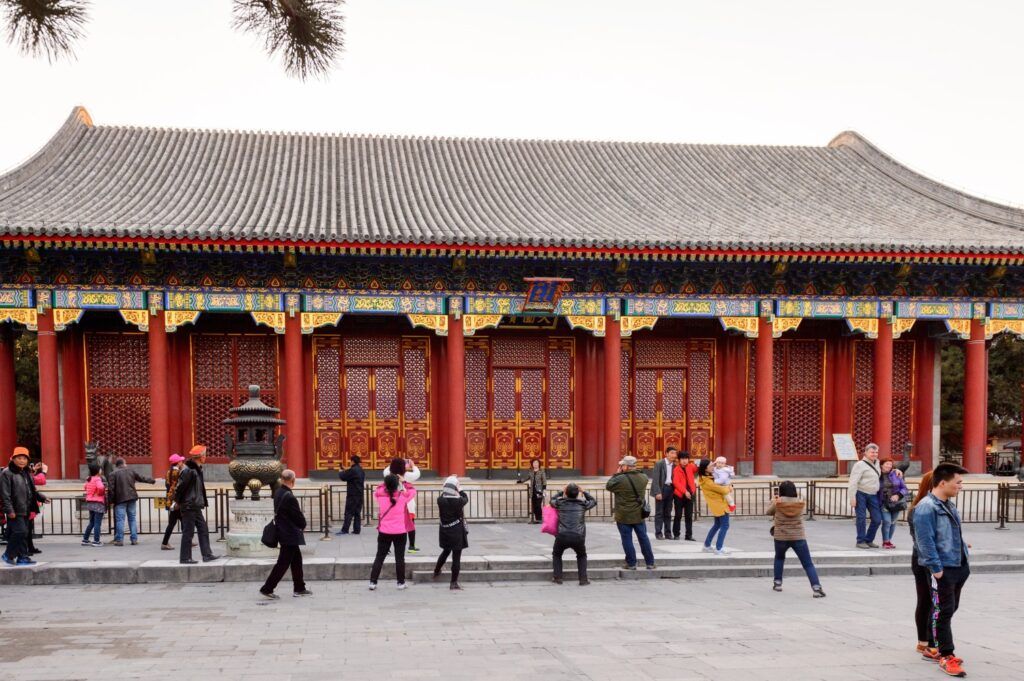 Exterior of a large red and gold building with a gray roof and people walking in the foreground
