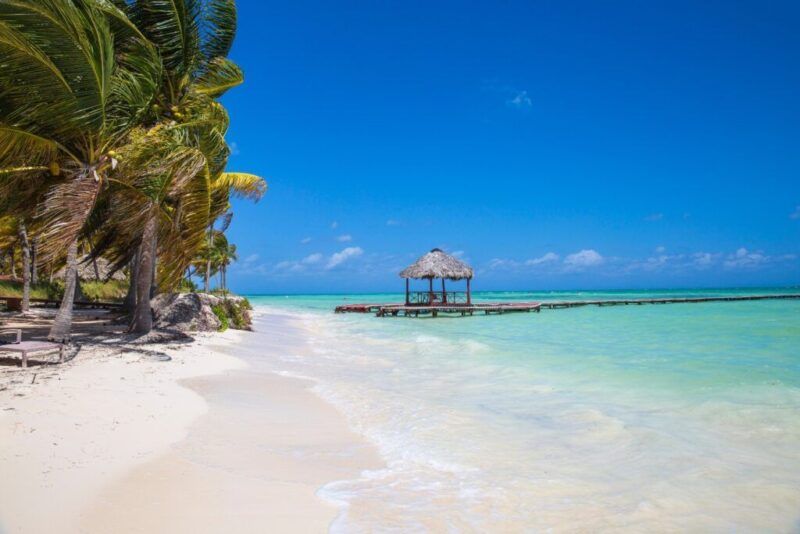 A white sand beach with turquoise waters and a small thatched-roof pier in Cayo Guillermo.