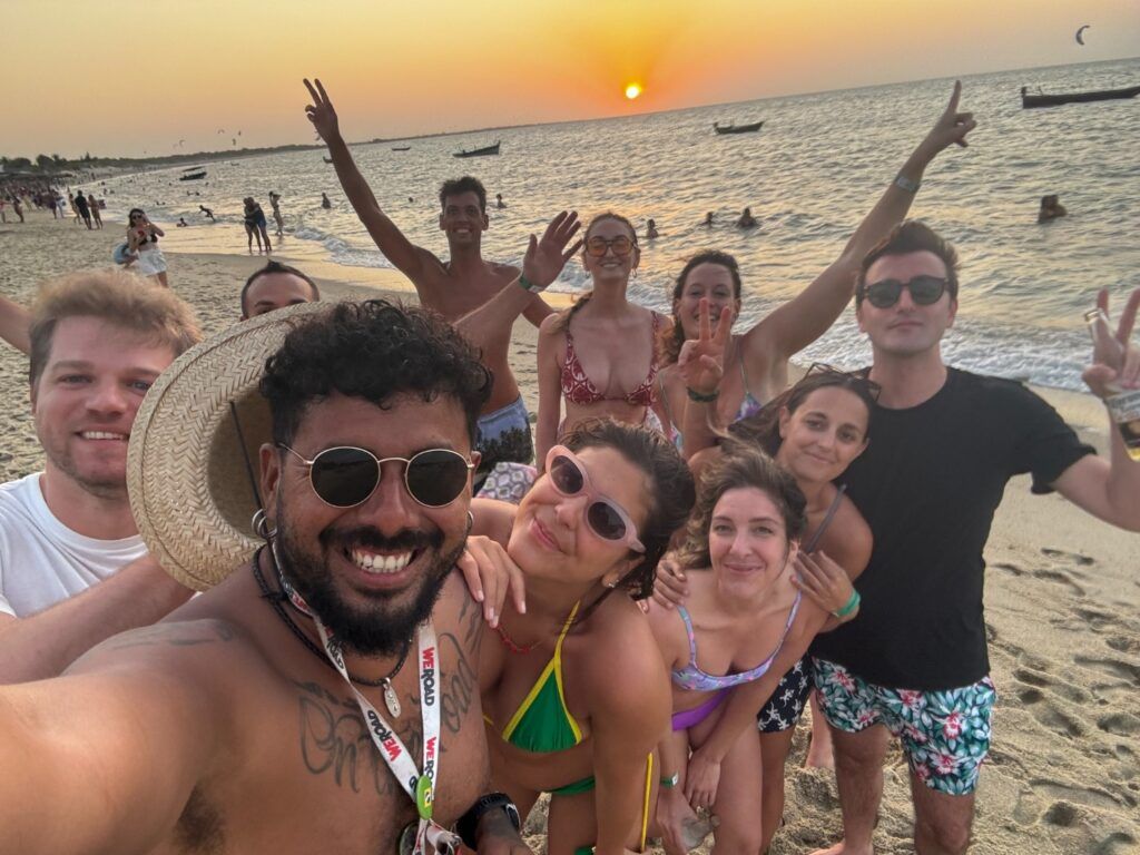 A group of happy WeRoad travelers taking a selfie on a Brazilian beach at sunset.