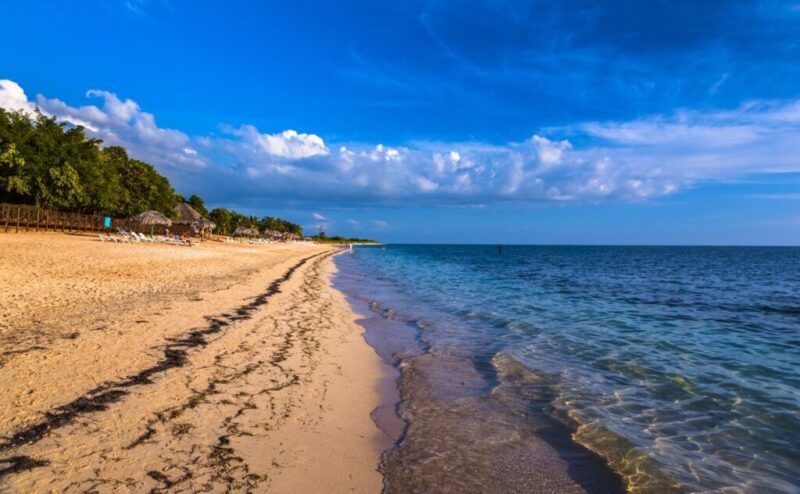 A tranquil view of the golden sands and clear blue waters of Playa Ancón in Cuba under a bright sky