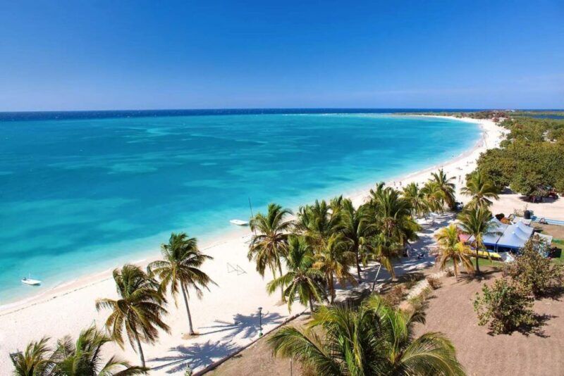 An aerial view of a pristine white sand beach with turquoise waters and palm trees in Cuba.