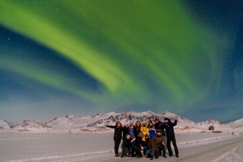 A group of WeRoad travelers watches the northern lights in Iceland under a spectacular sky filled with polar auroras.