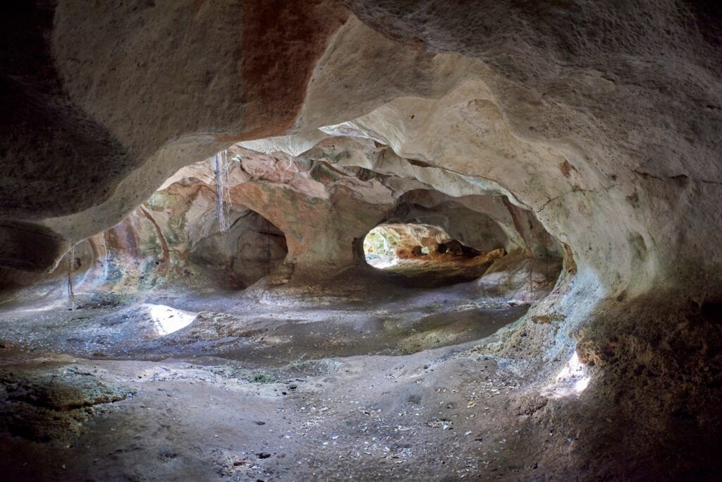 The interior of a natural limestone cave in Cuba with multiple rocky openings and sunlight filtering through.