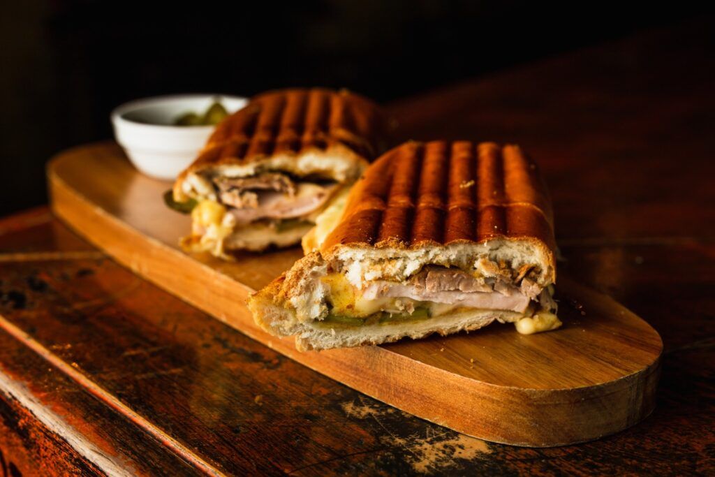 A sliced Cuban sandwich with roasted pork, ham, Swiss cheese, and pickles on a wooden serving board.