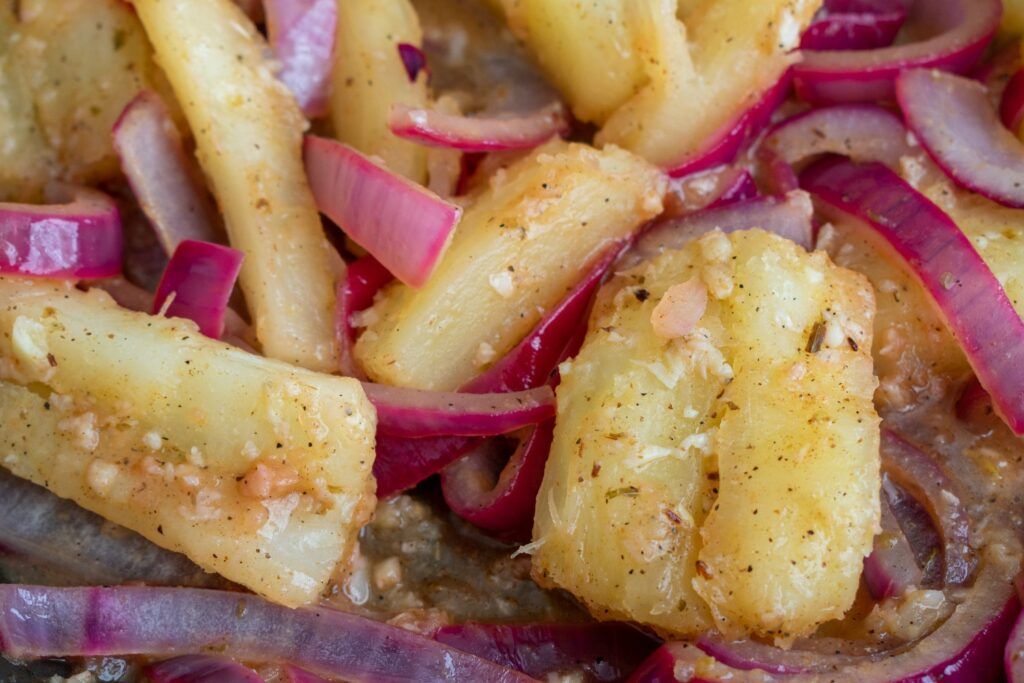 Close-up of Cuban-style boiled yuca con aliño, served with sautéed red onions and garlic.