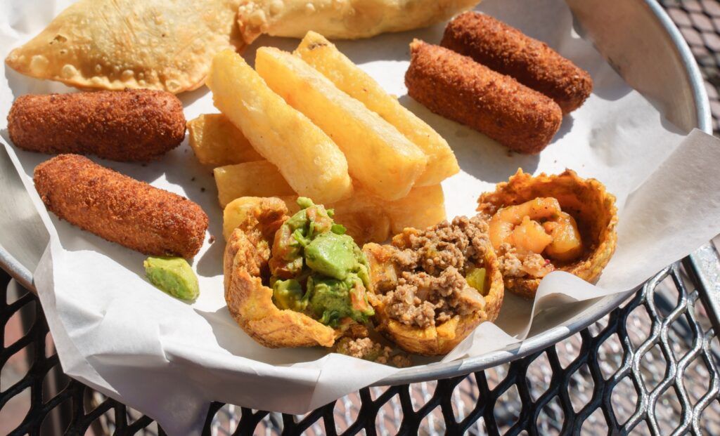 A platter of Cuban appetizers featuring croquettes, fried yuca, empanadas, and stuffed plantain cups (tostones rellenos).