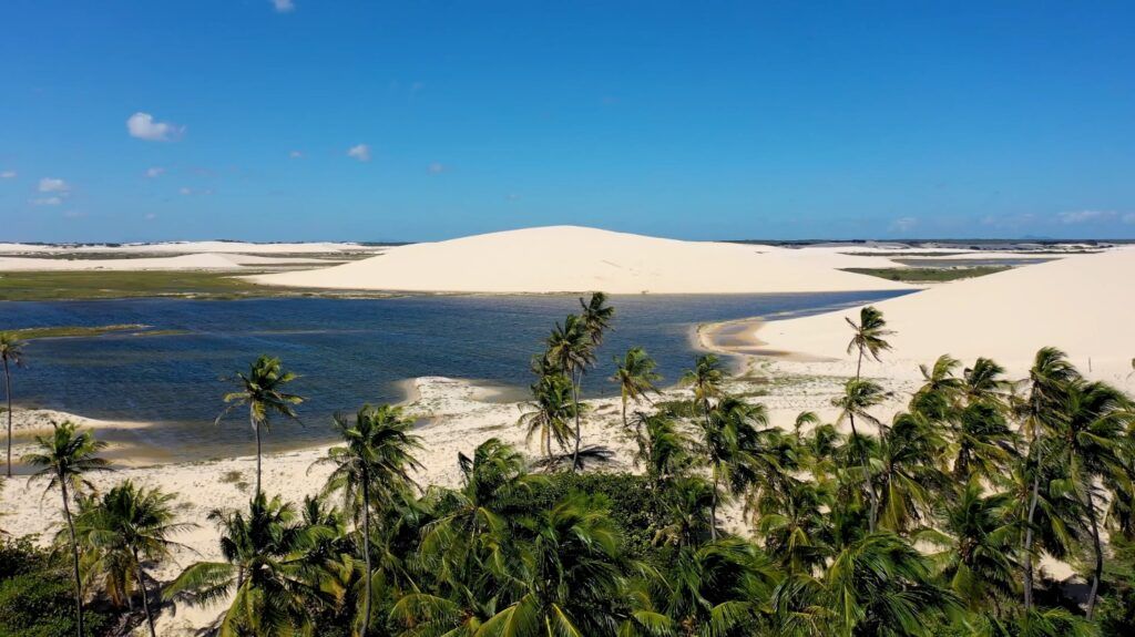 Panoramic view of a freshwater lagoon nestled between towering white sand dunes and green palm trees in Jericoacoara.